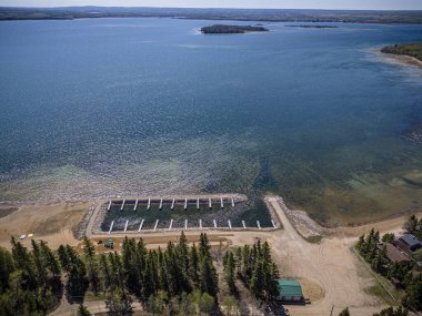 An aerial drone photo of Pebble Baye at Iroquois Lake, Saskatchewan, showcasing waterfront properties, lush greenery, the lake shoreline, and recreational areas in a serene summer setting. clipart