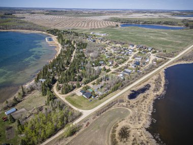 An aerial drone photo of Pebble Baye at Iroquois Lake, Saskatchewan, showcasing waterfront properties, lush greenery, the lake shoreline, and recreational areas in a serene summer setting. clipart