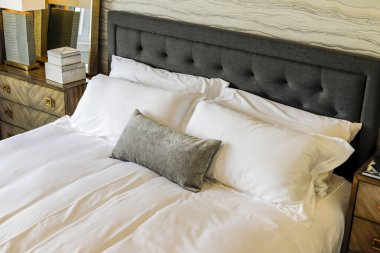 Gri yatak başlıklı ve beyaz yastıklı bir yatak. Yatak yapıldı ve çok rahat görünüyor.