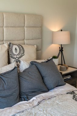 Beyaz yatak başlıklı ve mavi yastıklı bir yatak. Yastıklar denge ve uyum hissi yaratacak şekilde düzenlenmiştir. Sahne sakin ve huzurlu, izleyiciyi rahatlamaya ve gevşemeye davet ediyor.