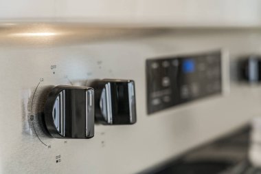 Solunda siyah bir düğmesi olan gümüş bir soba. Kapı tokmağı kapalı etiketli. Fırın kapalı.