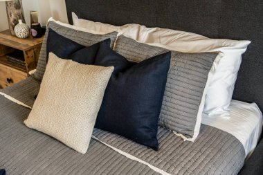 Beyaz yorganı ve siyah beyaz yastığı olan bir yatak. Yastık yatağın üstünde ve diğer yastıklarla çevrili.