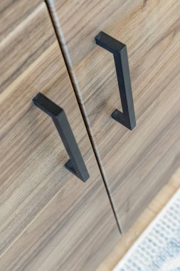 Dolap kapılarının kulpları siyah ve ahşaptan yapılmıştır. Dolap ahşaptan yapılmıştır ve kahverengi bir kapağı vardır.