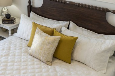 Beyaz yorgan ve sarı yastıklı bir yatak. Yastıklar denge ve uyum hissi yaratacak şekilde düzenlenmiştir. Yatak davetkar ve rahat, rahat bir atmosferi var.