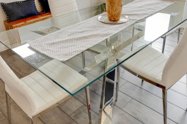 Üzerinde beyaz bir masa örtüsü ve bir vazo çiçek olan cam bir masa. Masa beyaz sandalyelerle çevrili.