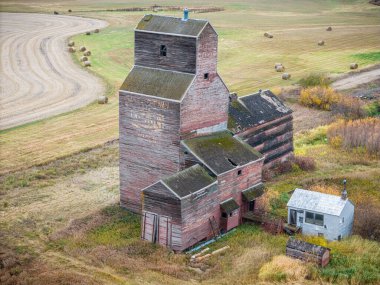 Eski bir kırmızı tahıl asansörü tarlada duruyor. Bina terk edilmiş ve bakımsız görünüyor.