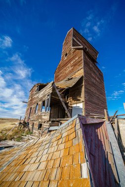 Kırmızı çatılı ve arka planında mavi gökyüzü olan harap olmuş eski bir bina. Bina terk edilmiş ve bakımsız görünüyor.