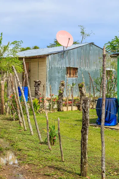Üzerinde uydu anteni olan küçük bir kulübe. Kulübenin etrafı çitlerle çevrili ve yerde mavi bir fıçı var.