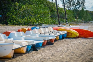 Sahilde bir sıra küçük tekne sıraya dizildi. Tekneler mavi, sarı ve beyaz olmak üzere farklı renklerdedir. Boş zaman ve rahatlama kavramı