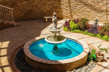 Ortasında bir çocuk heykeli olan küçük bir çeşme. Çeşme birçok bitkiyle çevrili bir bahçeyle çevrilidir.