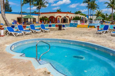 Mavi döşemeli ve beyaz tırabzanlı bir havuz. Havuzun etrafında birkaç şezlong var.