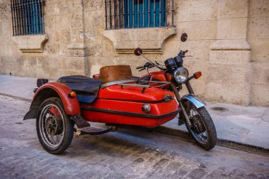 Sidecar 'ı olan kırmızı bir motosiklet caddeye park edilmiş. Motosiklet mavi pencereli bir binanın yanında park edilmiş.