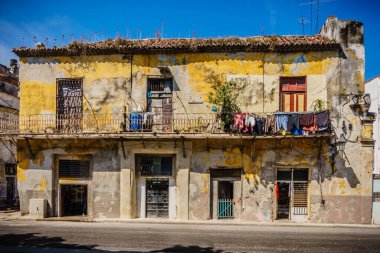 Üzerinde bir sürü giysi ve balkon olan sarı beyaz bir bina. Bina eski ve üzerinde bir sürü grafiti var.