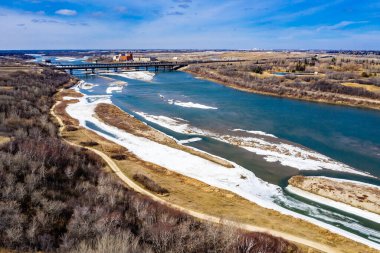 Arka planda köprü olan bir nehir. Su dondu ve toprak karla kaplandı.