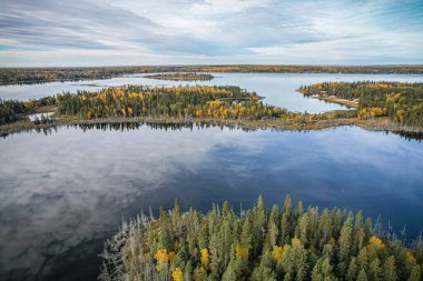 Arkasında ağaçlar ve adalar olan güzel bir göl manzarası. Gökyüzü bulutlu ve su sakin.