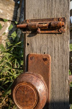 Paslı eski bir kapı tokmağı ahşap bir direğe oturur. Kapı kolu eski ve paslı, ve bakımsız. Görüntüde melankolik bir hava var.