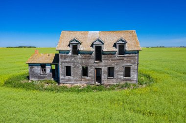 Büyük, eski bir ev bir çim tarlasında duruyor. Ev yeşil bir tarla ile çevrili ve terk edilmiş.