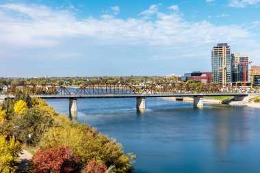 Bir köprü, arka planda bir şehir olan bir nehri kapsar. Köprü kırmızı ve sarı renkli bir metal yapıdır. Şehir hareketle dolup taşıyor.