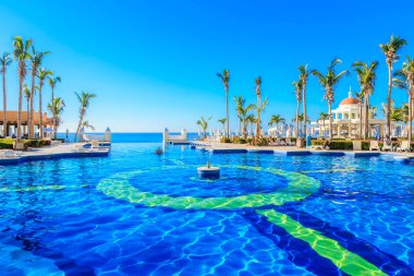 Ortasında çeşme, arkasında palmiye ağacı olan bir havuz. Havuz beyaz bir çitle çevrili.