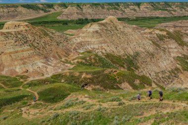 Bir grup insan çölde bir tepeye tırmanıyor. Manzara kayalık ve çorak, görünürde ağaç ya da bitki örtüsü yok. Gökyüzü açık ve mavidir ve güneş ışıl ışıl parlar.