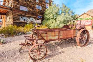 Eski, paslı bir çiftlik arabası üzerinde Coca-Cola işareti olan bir binanın önünde duruyor.