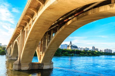 Bir köprü, arka planda bir şehir olan bir nehri kapsar. Köprü büyük bir kemer ve su sakin.