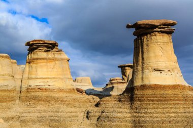 Arka planda bulutlu bir gökyüzü olan bir grup kaya oluşumu. Düzen uzundur ve benzersiz bir şekle sahiptir. Sahneye huzurlu ve huzurlu bir atmosfer verir. Bulutlu gökyüzü derinlik katıyor