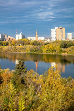 İçinden nehir akan bir şehir silueti. Gökyüzü bulutlu ve güneş batıyor.
