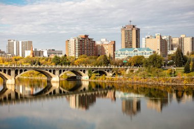 Üzerinden bir nehir akan ve üzerinde bir köprü olan bir şehir. Köprü suya yansıyor.
