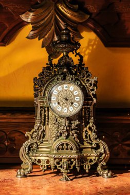 A large, ornate clock with a gold frame sits on a table. The clock has a gold face and hands, and the numbers are black. The clock is surrounded by a decorative frame, which adds to its elegance clipart