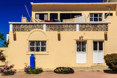Üzerinde mavi su tankı olan sarı bir ev. Evde balkon, çamaşır makinesi ve kurutma makinesi var.