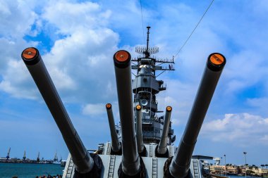 Önünde üç büyük top olan büyük bir savaş gemisi. Gökyüzü mavi ve bazı bulutlar var.