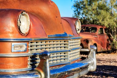 Paslı kapüşonlu eski bir araba çölde duruyor. Araba ağaçlar ve kayalarla çevrili.