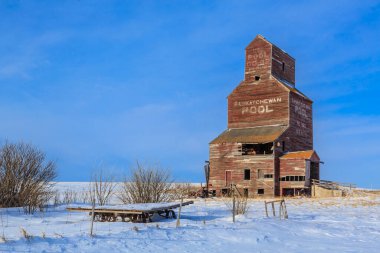 Karlı bir tarlada büyük, eski, kırmızı bir tahıl ambarı bulunuyor. Silo boş ve gökyüzü temiz.