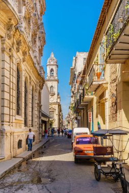 Kırmızı arabası ve bisikleti olan bir sokak sahnesi. Araba yolun kenarına park edildi ve bisiklet onun yanına park edildi. Sokakta yürüyen birkaç kişi var.