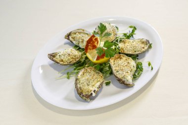 Üzerine limon dilimi ve maydanoz konmuş bir tabak istiridye. Tabak beyaz ve istiridyeler dairesel bir düzende dizilmiş.