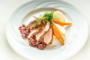 Üzerinde bir parça et ve havuç olan bir tabak yemek. Tabak beyaz ve yemek renkli.