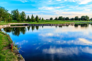 Arka planda golf sahası olan bir göl. Su sakin ve gökyüzü mavi.