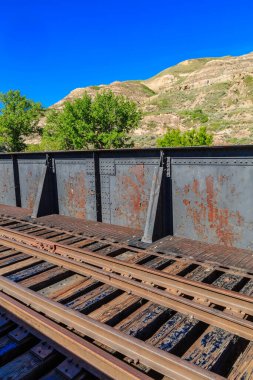 Tren rayları paslı ve eski, arkasında mavi bir gökyüzü var. Manzara biraz melankoliktir, eski tren rayları eski bir çağın hatırlatıcısı gibi görünür.