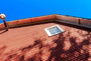 Penceresi ve çatısında lamba olan kırmızı bir ev. Işık evin çatısında, alttaki alanı aydınlatıyor. Evin ahşap kaplamalı, eski moda bir görünüşü var.