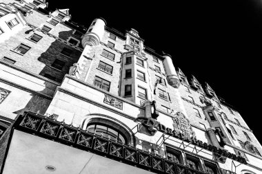 Bir sürü penceresi olan bir binanın siyah beyaz fotoğrafı. Bina çok yüksek ve çok fazla detaya sahip. Fotoğrafın karamsar ve dramatik bir havası var.