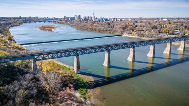 Bir köprü, arka planda bir şehir olan bir nehri kapsar. Köprü metalden yapılmıştır ve uzun bir mesafe kateder.
