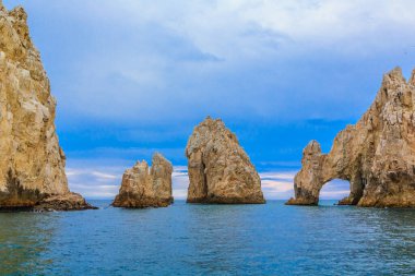 Üzerinde mavi bir gökyüzü olan kayalık bir kıyı şeridi. Kayalar kıyı şeridi boyunca dağılmış ve su sakin. Manzara huzurlu ve huzurlu, güzel mavi gökyüzü