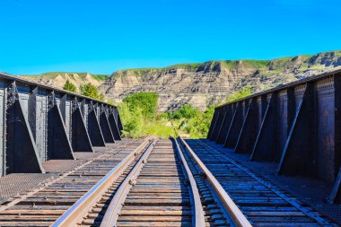 Tren rayları eski ve paslı ve köprü de metalden yapılmış. Arkadaki dağların manzarası nefes kesici.