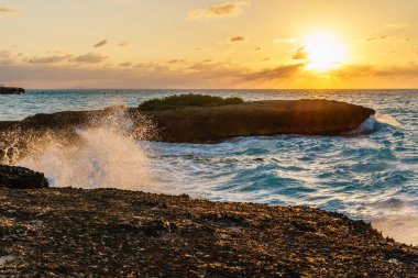 Okyanus sakin ve güneş batıyor. Su koyu mavi bir renktir. Gökyüzü turuncu ve pembe karışımıdır.
