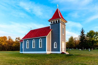 Kırmızı çatılı küçük mavi bir kilise. Kilise çimenli bir tarla ile çevrilidir. Gökyüzü mavi ve berrak