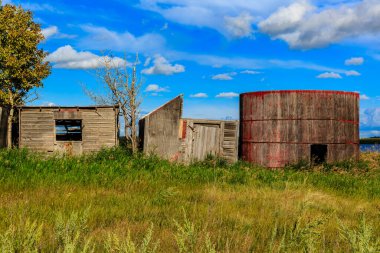 Kırmızı çatılı bir ahır ve pencereli bir kulübe. Ahır eski ve kulübe bir tarlada.