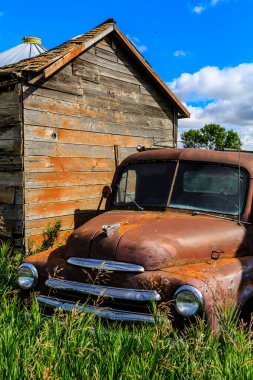Ahırın yanındaki tarlada eski bir kamyon var. Kamyon paslanmış ve soluk kırmızı bir rengi var. Ahır ahşaptan yapılmıştır ve eğimli bir çatısı vardır.