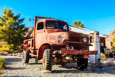 Eski bir kırmızı kamyon bir binanın önünde park edilmiş. Kamyon paslanmış ve üzerinde bir sürü kir var.
