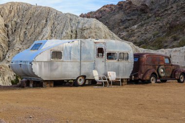Paslı eski bir kamyonun yanına gümüş renkli bir karavan park edilmiş. Karavan eski ve paslı ayrıca kamyon da eski ve paslı. Sahnenin nostaljik ve melankolik bir havası var.